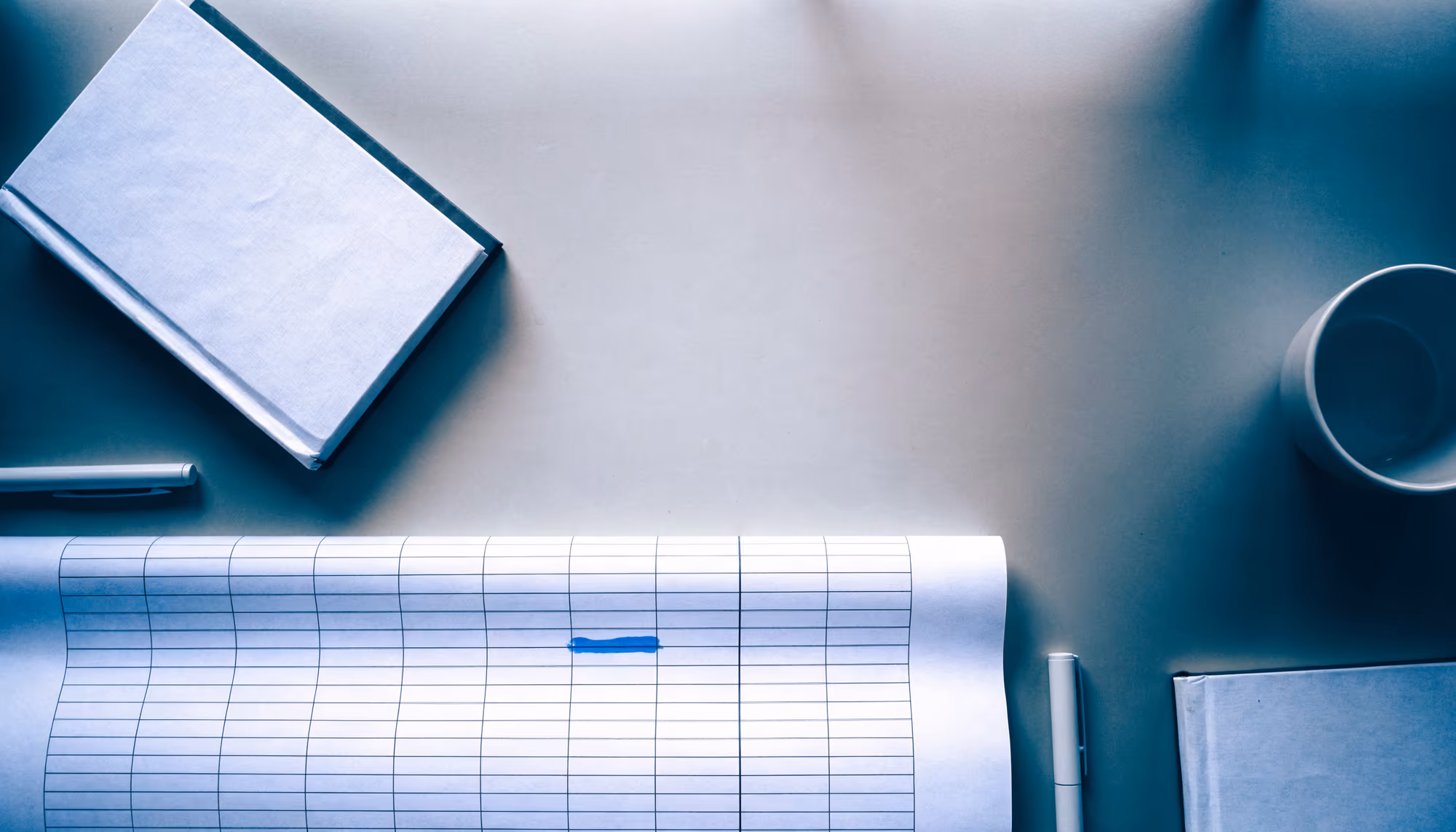 An overhead view of a long printed schedule laid across a desk between two closed notebooks, one bar marked in blue.
